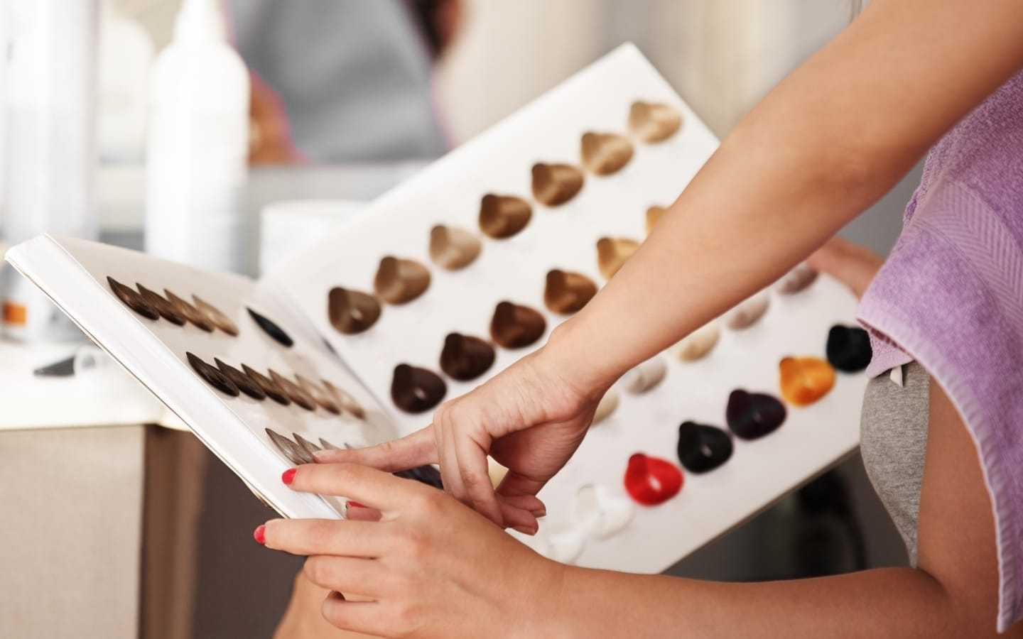 Person selecting hair color from a sample book in a salon setting.