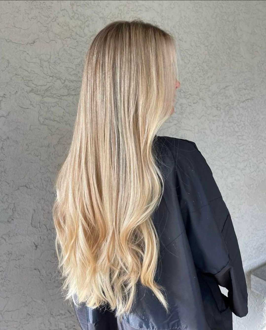 Blonde-haired person in black jacket, back view against a textured gray wall.