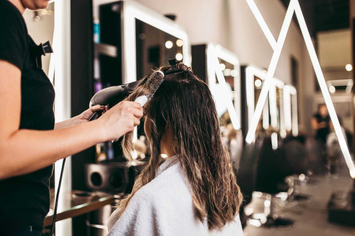 Hairdresser blow-drying a woman's hair in a modern salon setting.