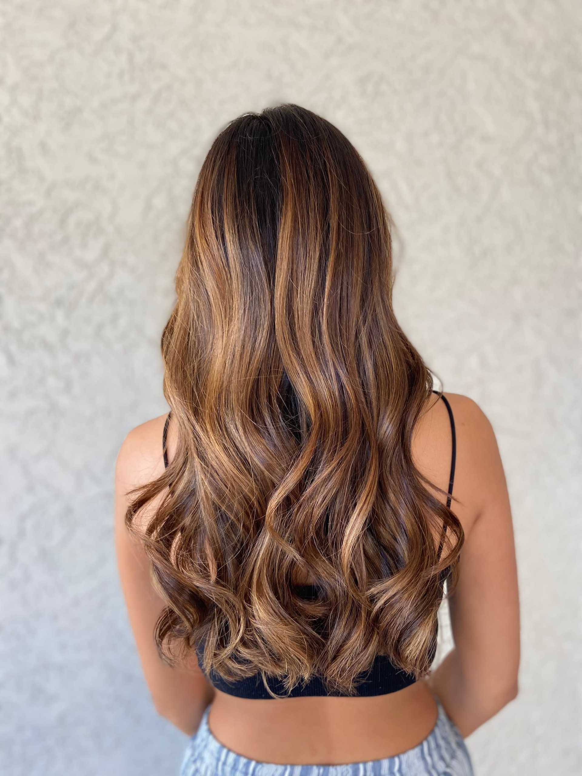 Woman with long, curly brown hair facing away, wearing a black top.